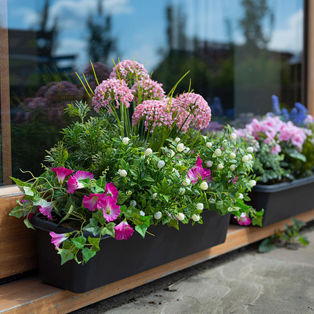 Faux pink flowers in planters beside window