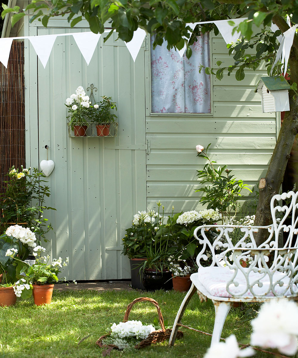 Green painted shed in garden with white bunting and flowers